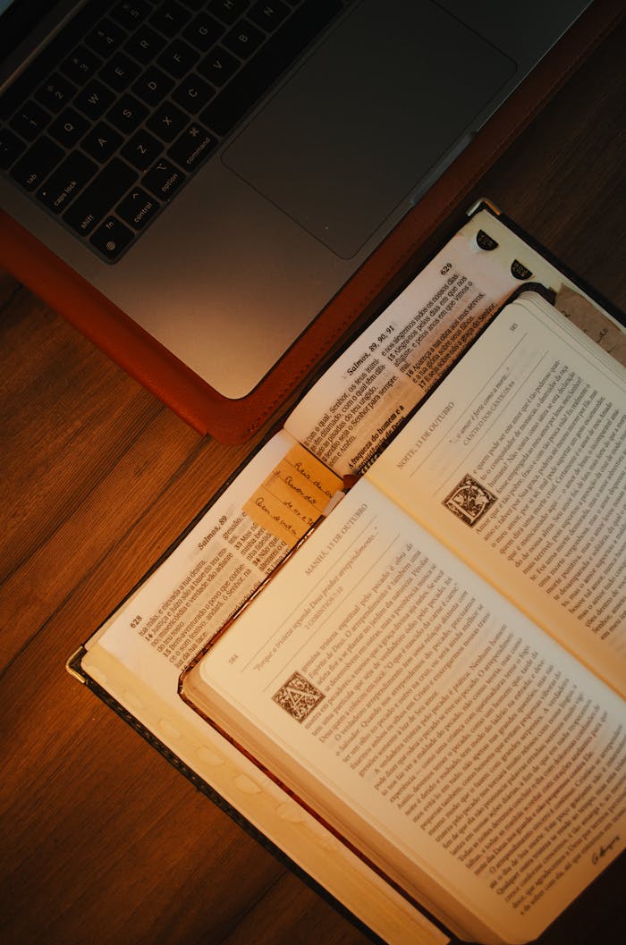 A cozy scene with an open book and laptop on a wooden desk, perfect for study or work.