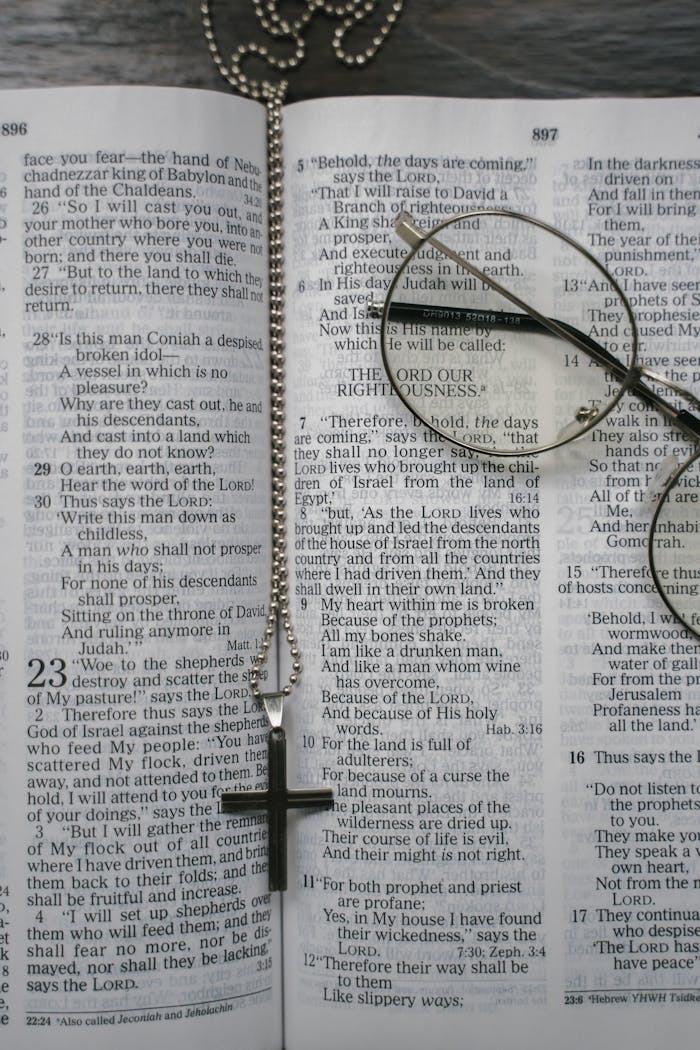 An open Bible with a cross necklace and glasses placed on the pages, symbolizing faith.