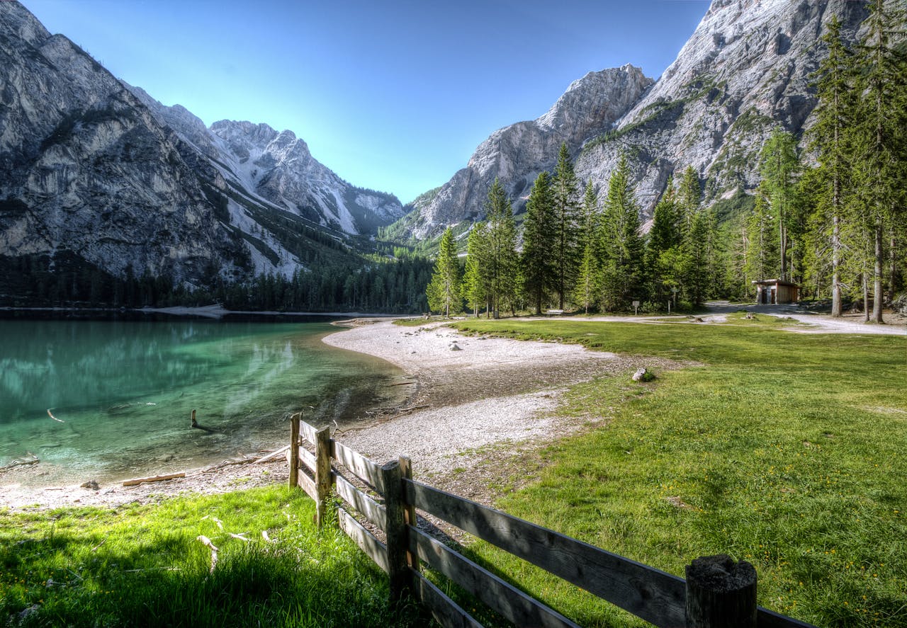 Serene mountain lake with green trees and a rustic fence, perfect nature backdrop.